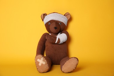 Photo of Toy bear with bandages on yellow background