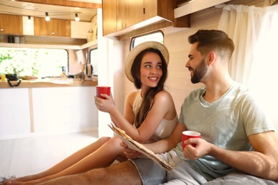 Photo of Happy young couple with cups and newspaper in trailer. Camping vacation