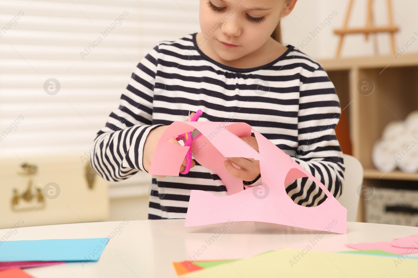 Photo of Girl cutting pink paper at desk in room, closeup. Home workplace