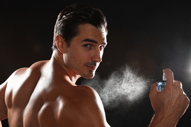 Handsome young man applying perfume on black background