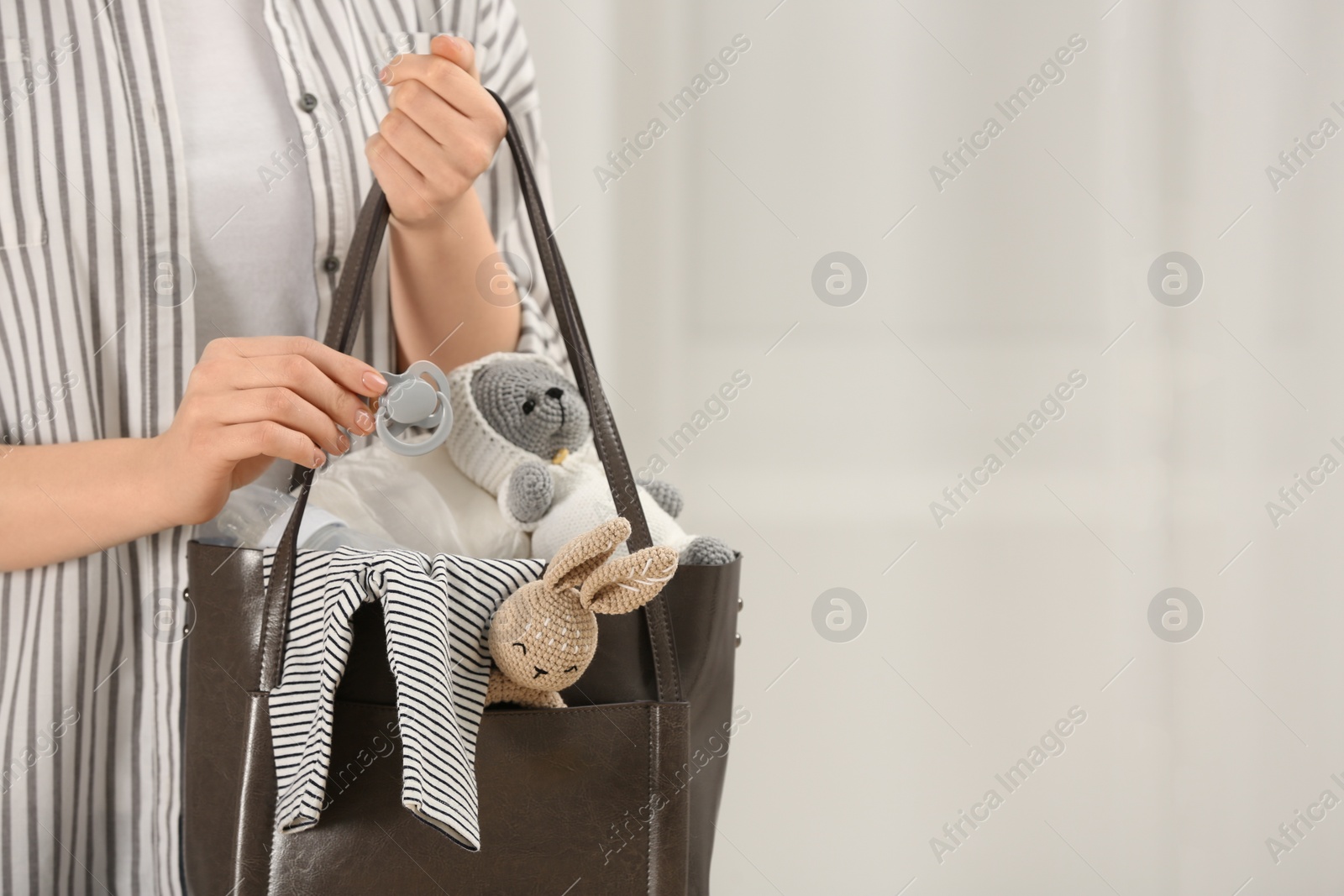 Photo of Woman putting pacifier into mother`s bag indoors, closeup. Space for text