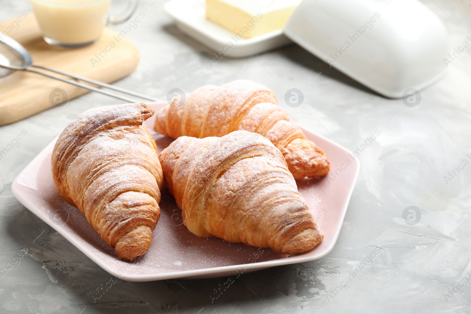 Photo of Plate of fresh croissants sprinkled with powdered sugar on grey table. French pastry