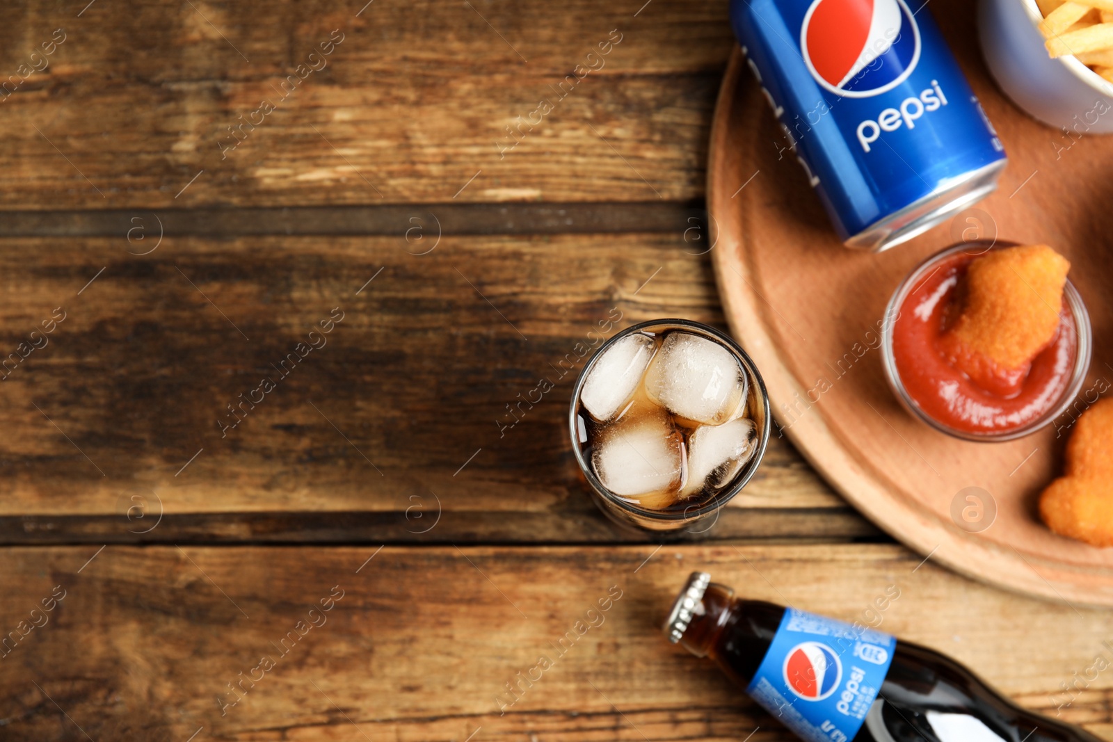 Photo of MYKOLAIV, UKRAINE - FEBRUARY 15, 2021: Different Pepsi drinks and snacks on wooden table, flat lay. Space for text