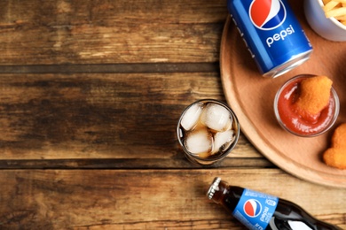 MYKOLAIV, UKRAINE - FEBRUARY 15, 2021: Different Pepsi drinks and snacks on wooden table, flat lay. Space for text