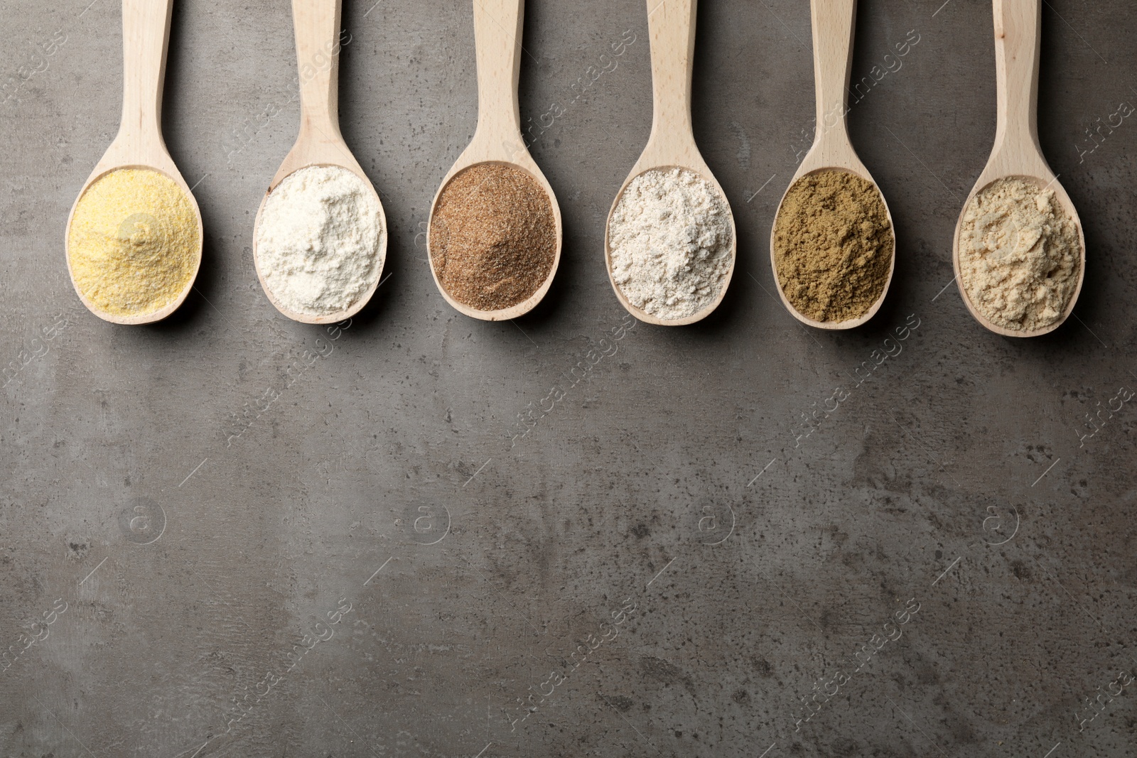 Photo of Spoons with different types of flour on grey background, top view. Space for text