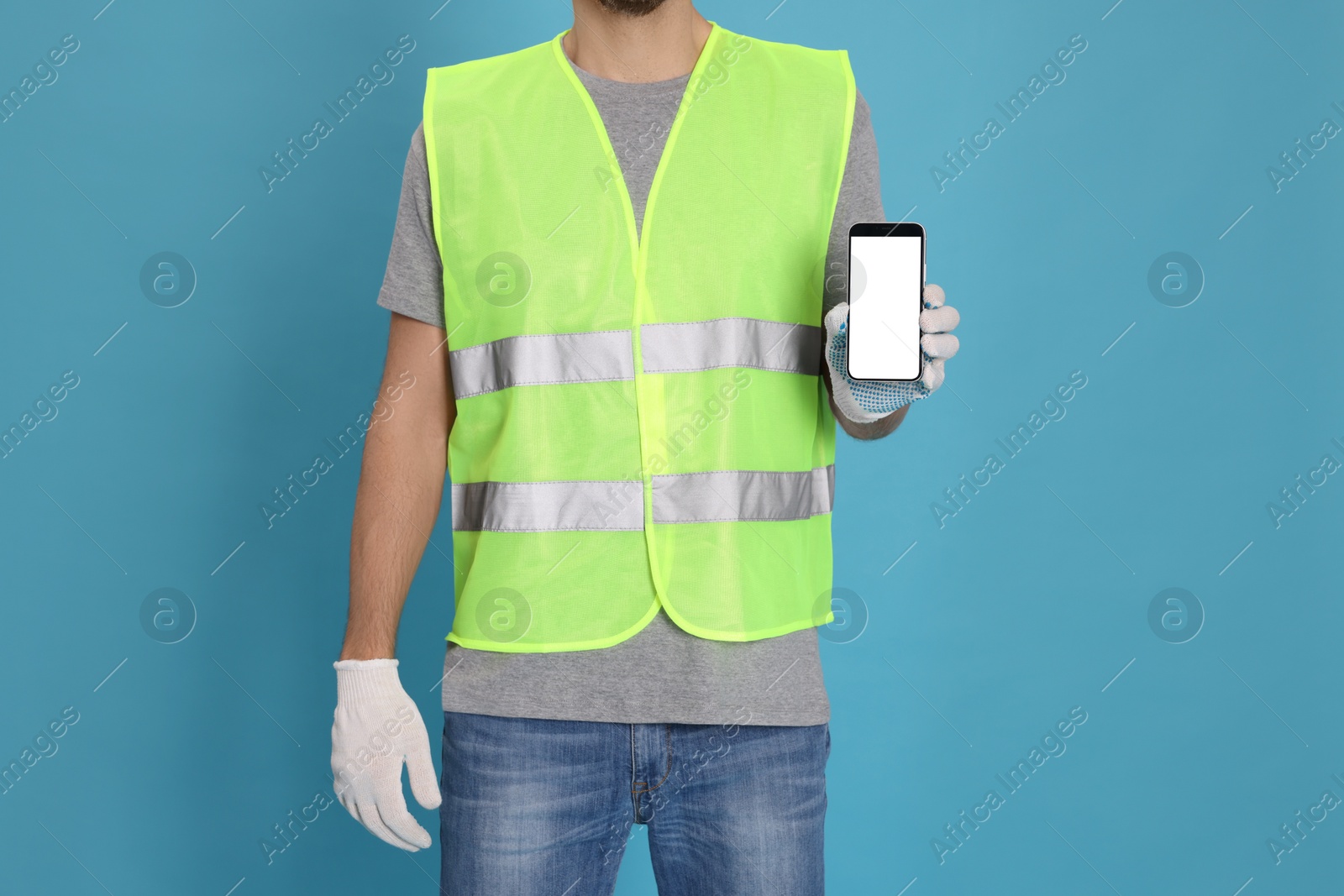 Photo of Male industrial engineer in uniform with phone on light blue background, closeup