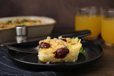 Photo of Tasty sausage casserole with green onions and cutlery served on wooden table, closeup