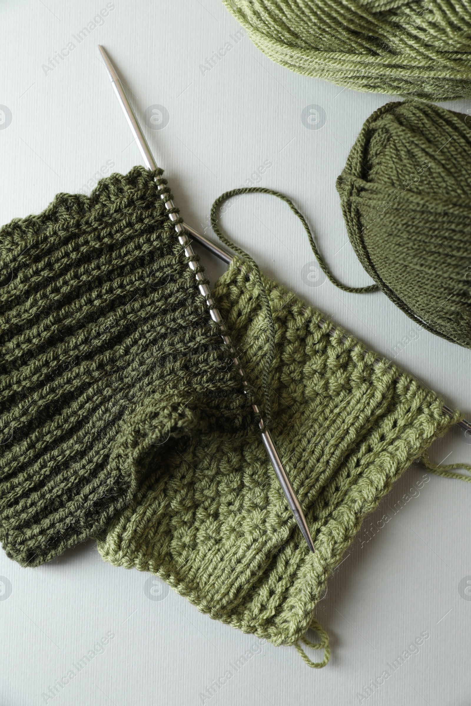 Photo of Green knitting, needles and soft yarns on light background, flat lay