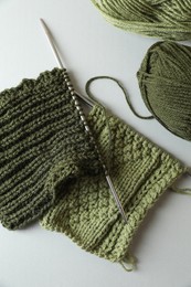 Photo of Green knitting, needles and soft yarns on light background, flat lay