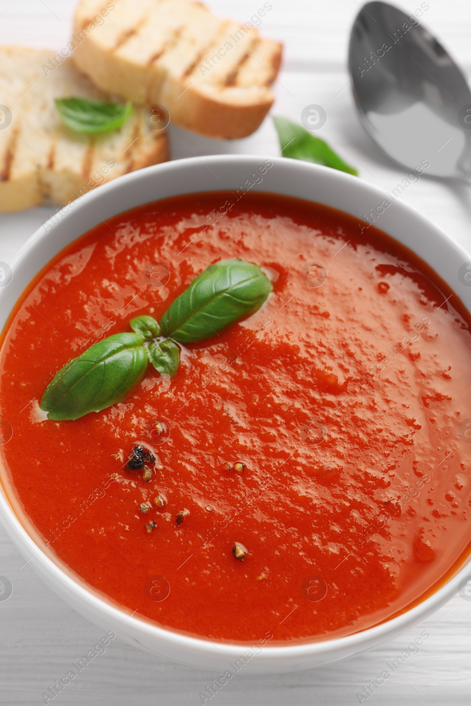 Photo of Delicious tomato cream soup in bowl on white wooden table, closeup