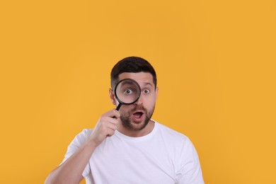 Surprised man looking through magnifier glass on yellow background