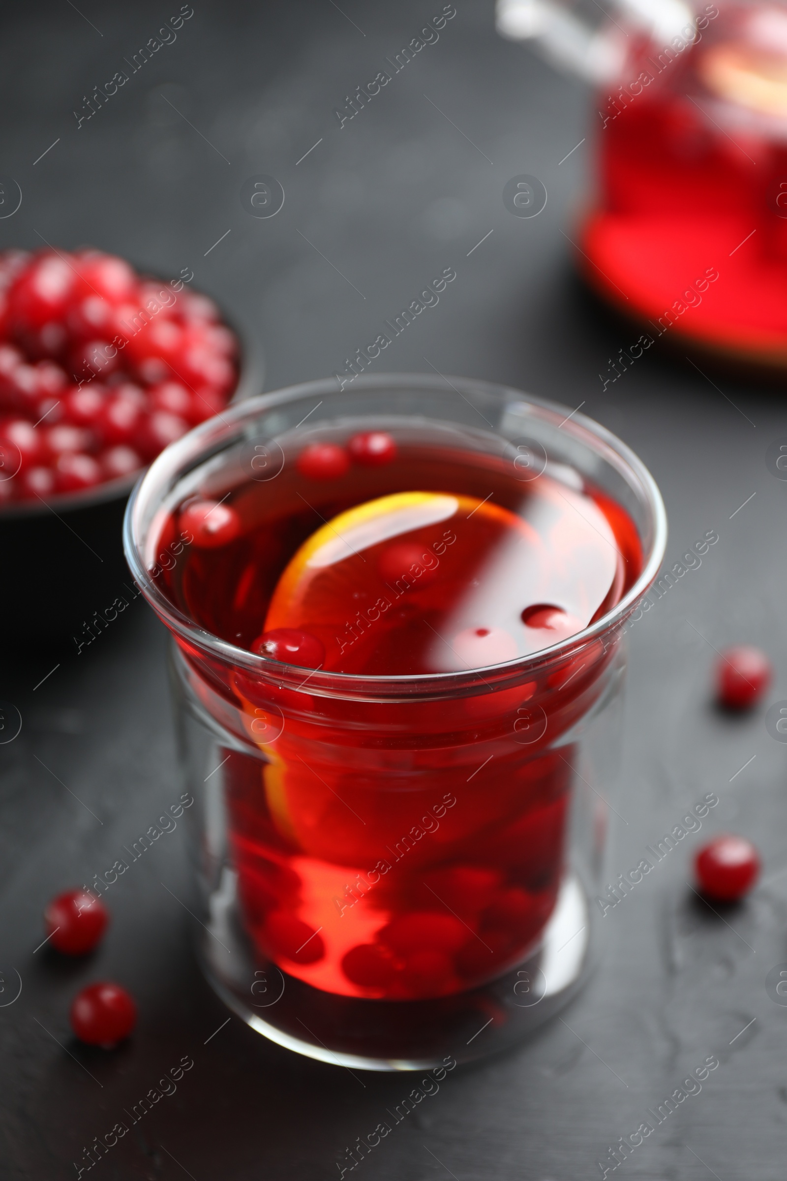 Photo of Tasty hot cranberry tea with lemon and fresh berries in glass on black textured table