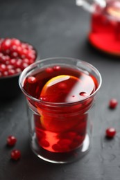 Tasty hot cranberry tea with lemon and fresh berries in glass on black textured table