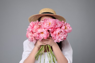 Young woman covering her face with bouquet of peonies on grey background