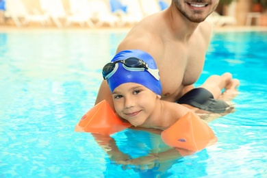 Happy father teaching his son to swim with inflatable sleeves in pool