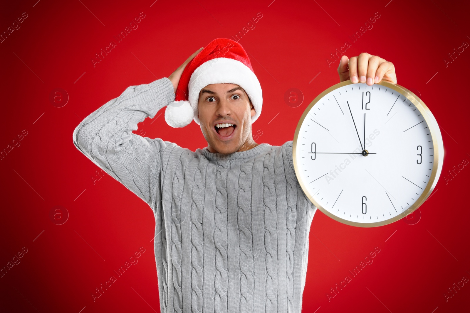 Photo of Man in Santa hat with clock on red background. New Year countdown