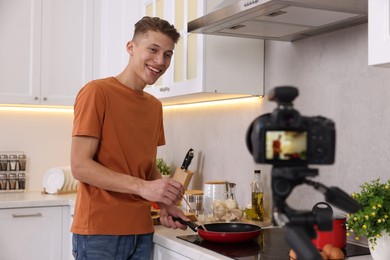 Photo of Smiling food blogger cooking while recording video in kitchen