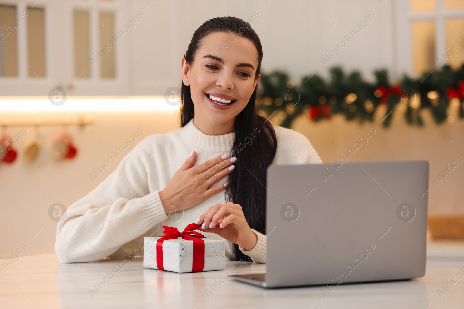Photo of Celebrating Christmas online with exchanged by mail presents. Smiling woman thanking for gift during video call at home