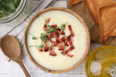 Photo of Delicious potato soup with bacon and microgreens in bowl served on wooden table, flat lay