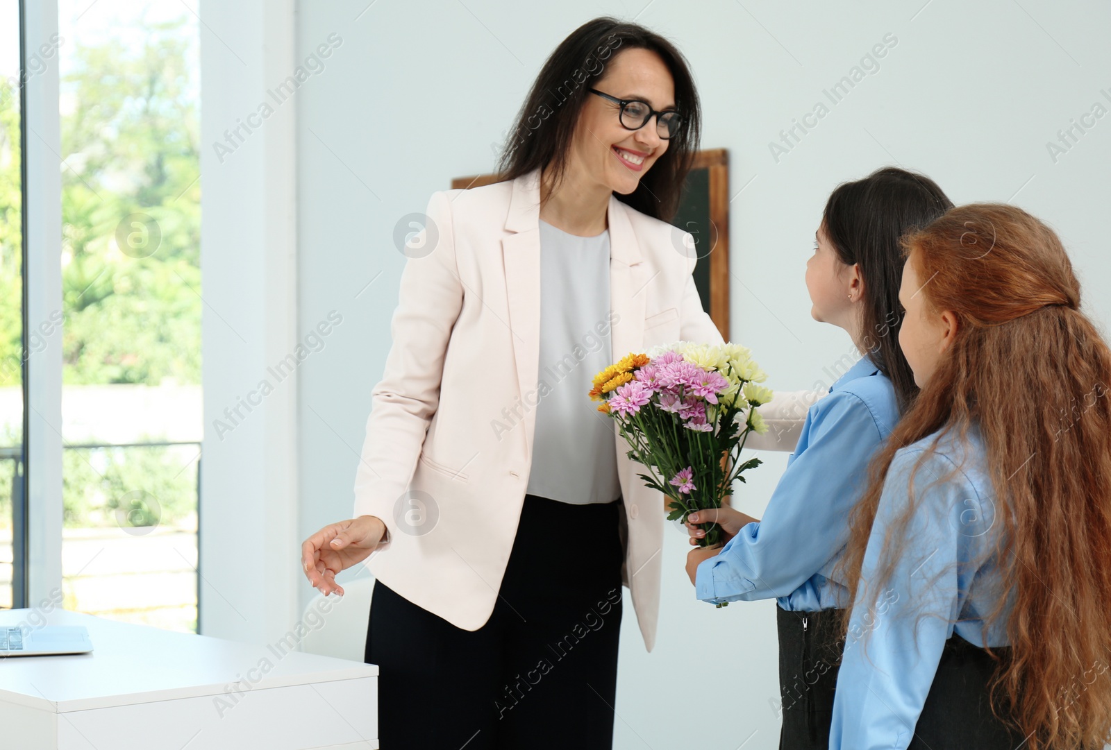 Photo of Schoolgirls with bouquet congratulating their pedagogue in classroom. Teacher's day