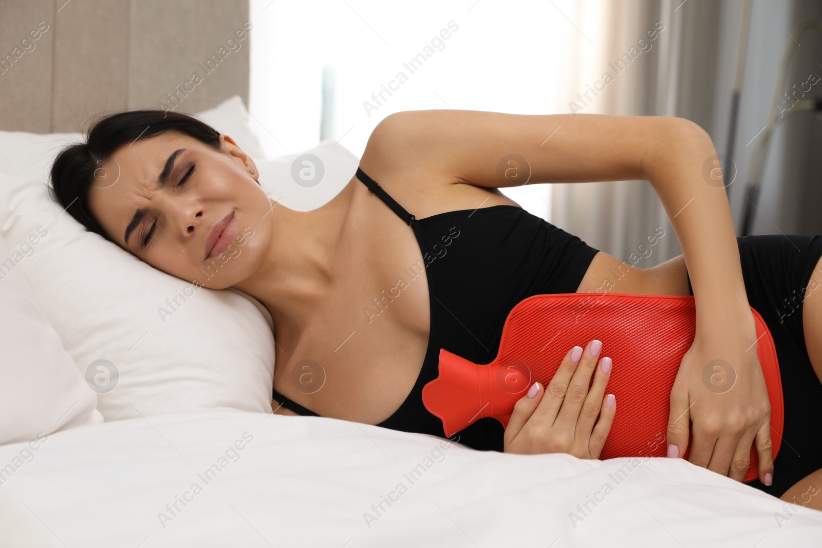 Photo of Woman using hot water bottle to relieve menstrual pain on bed at home