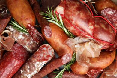 Different types of sausages with rosemary as background, flat lay