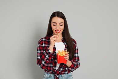 Photo of Beautiful young woman eating French fries on grey background