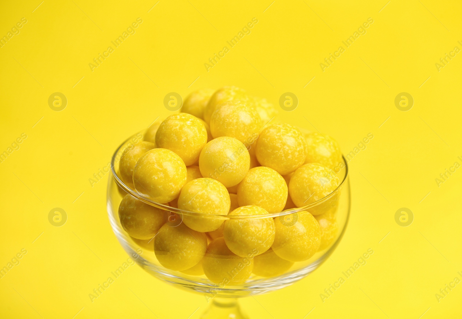 Photo of Tasty lemon chewing gums in glass on yellow background