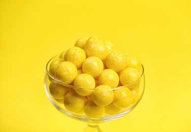 Photo of Tasty lemon chewing gums in glass on yellow background