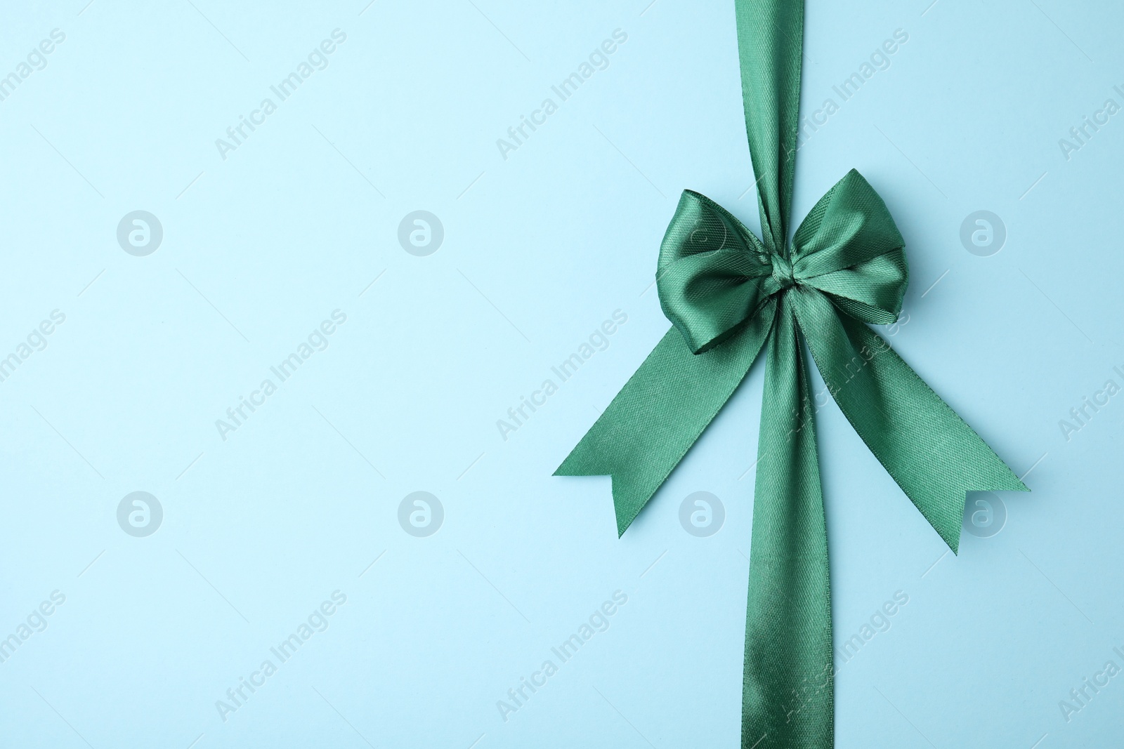 Photo of Green satin ribbon with bow on light blue background, top view