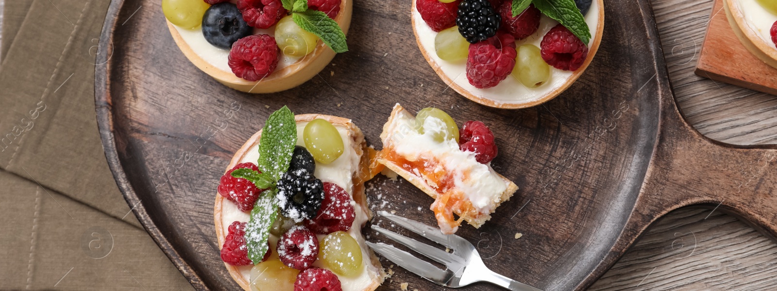 Image of Delicious tartlets with berries on wooden table, flat lay. Banner design