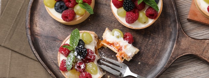 Image of Delicious tartlets with berries on wooden table, flat lay. Banner design