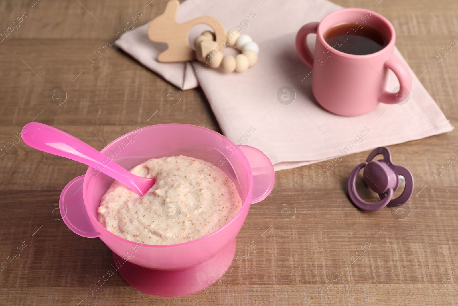 Photo of Baby food. Puree in bowl, drink, toy and soother on wooden table