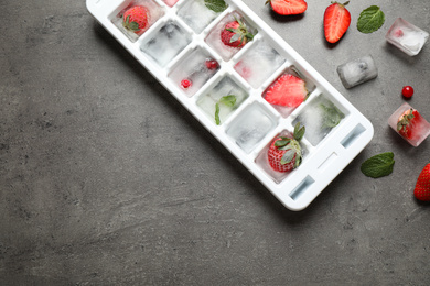 Ice cubes with berries and tray on grey table, flat lay