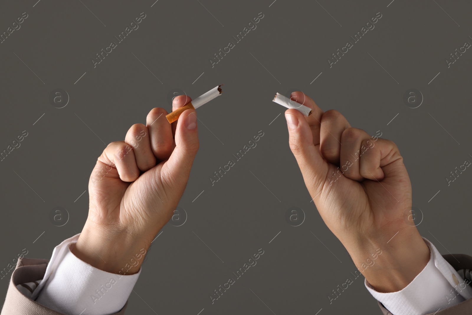 Photo of Stop smoking concept. Man holding pieces of broken cigarette on gray background, closeup