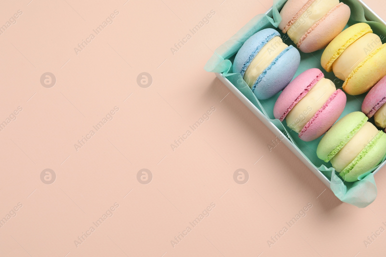 Photo of Many delicious colorful macarons in box on pink background, top view. Space for text