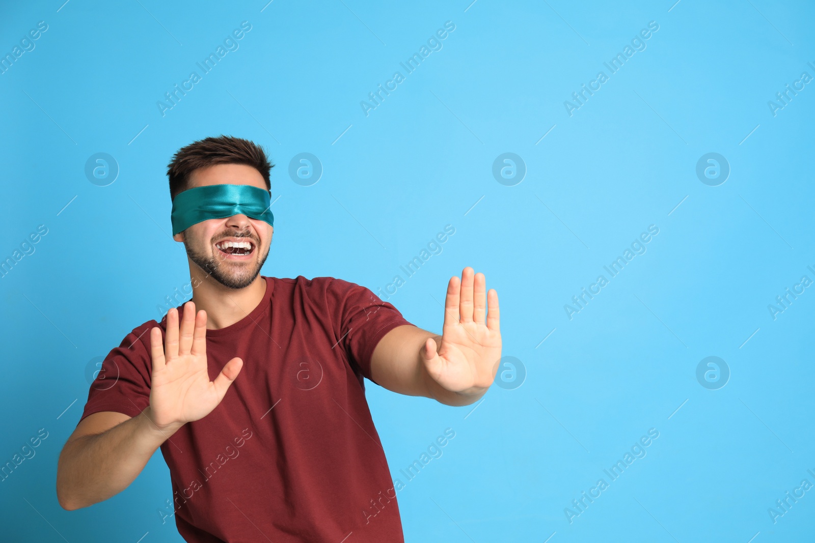 Photo of Young man with blindfold on blue background, space for text