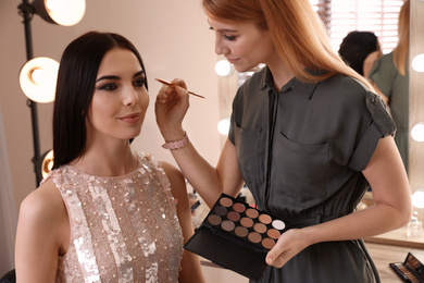 Photo of Professional makeup artist working with beautiful woman in salon