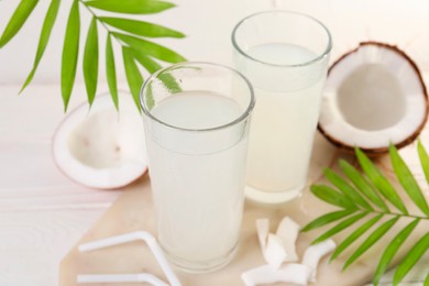 Photo of Glasses of coconut water, palm leaves and nuts on white table