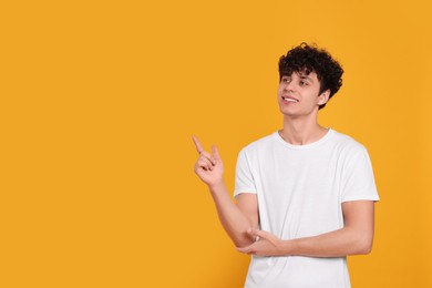 Handsome young man pointing at something on orange background. Space for text