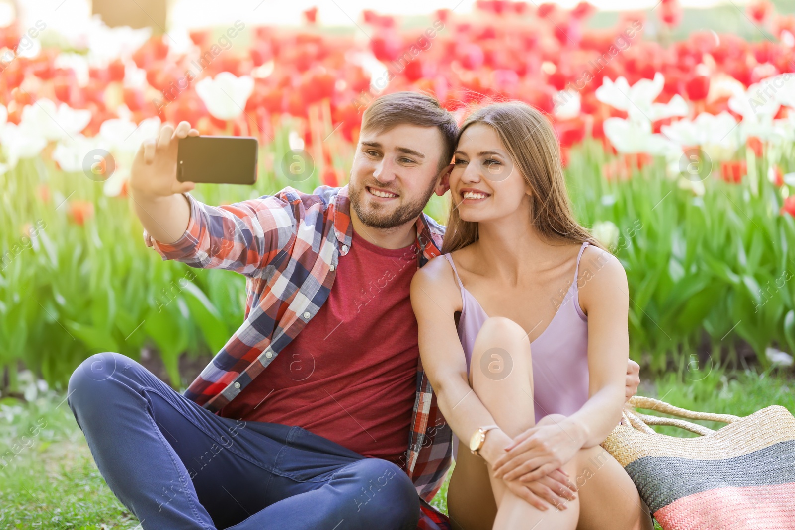 Photo of Happy young couple taking selfie in green park on sunny spring day