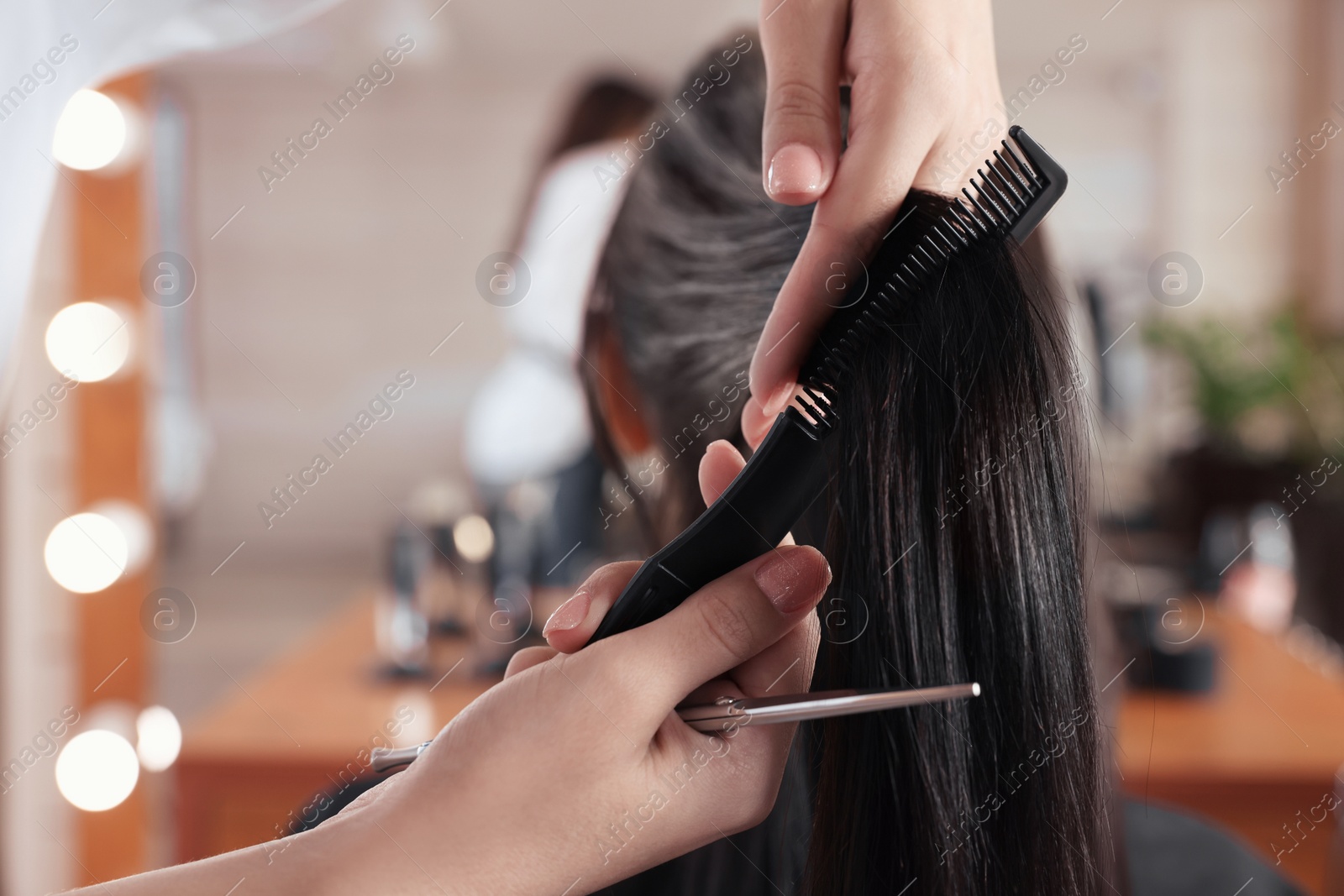 Photo of Professional hairdresser brushing woman's hair in beauty salon, closeup