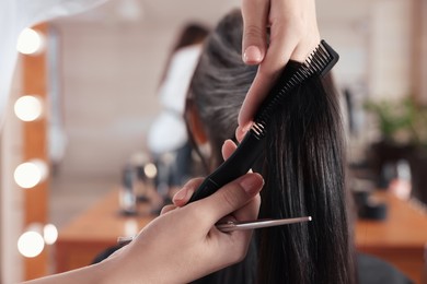 Photo of Professional hairdresser brushing woman's hair in beauty salon, closeup