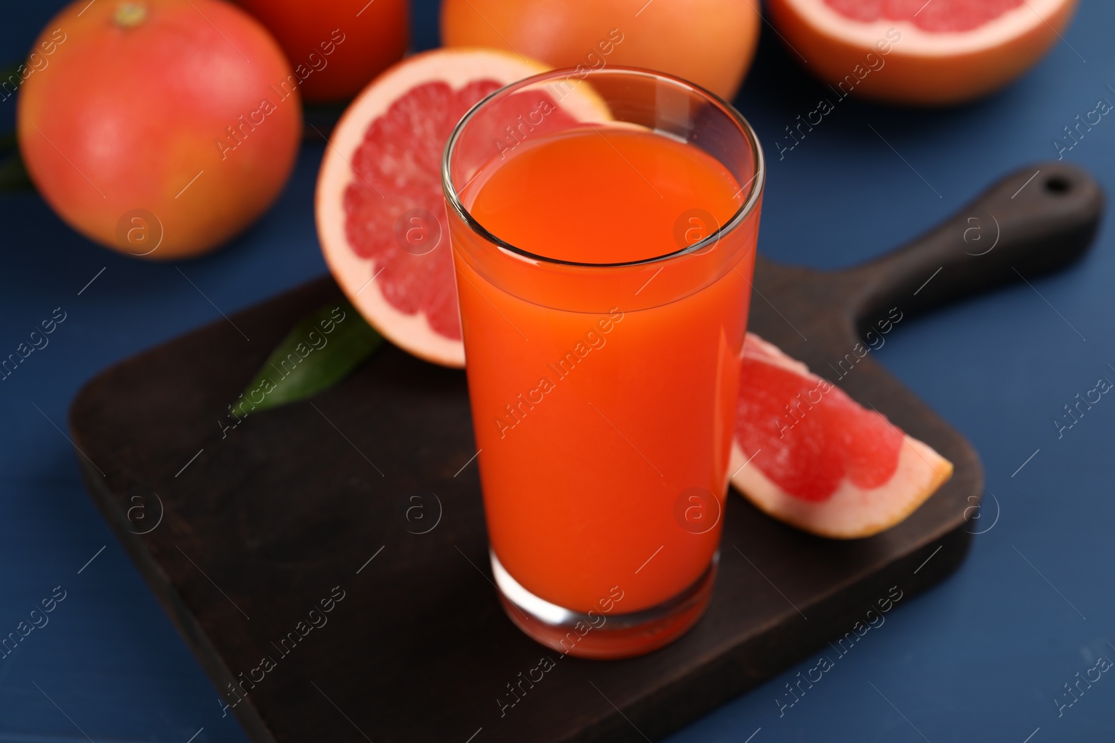 Photo of Tasty grapefruit juice in glass and fresh fruits on blue table, closeup