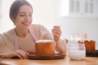 Photo of Young woman decorating traditional Easter cake with glaze in kitchen. Space for text