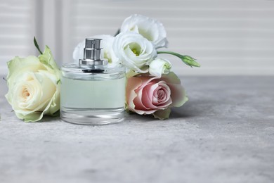 Bottle of perfume and flowers on grey table indoors
