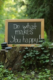 Photo of Chalkboard with phrase Do What Makes You Happy on stump outdoors