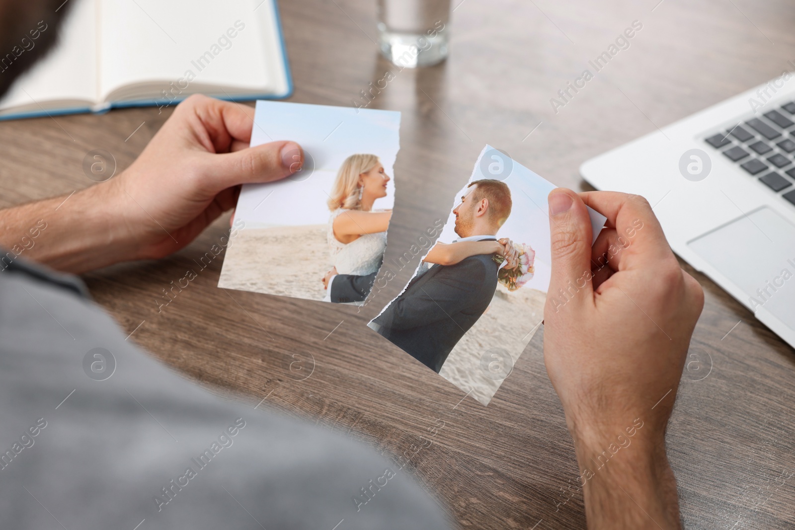 Photo of Man holding parts of photo at table indoors, closeup. Divorce concept