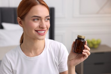 Photo of Happy young woman with bottle of pills in room, space for text. Weight loss