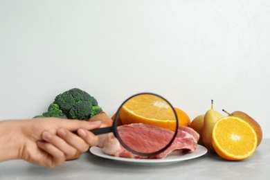 Photo of Woman with magnifying glass exploring raw meat and fruits, space for text. Poison detection